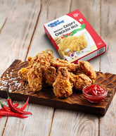 Crispy chicken pieces on a wooden board with a box of Crust N Crumb Crispy Chicken Mix - hot & spicy and a small bowl of ketchup.